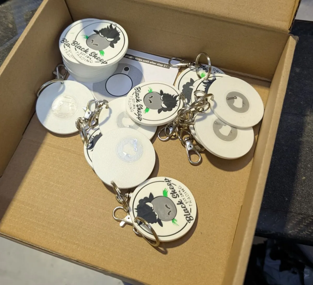 A box of finished keychains, some face down showing the NFC tag set into the back