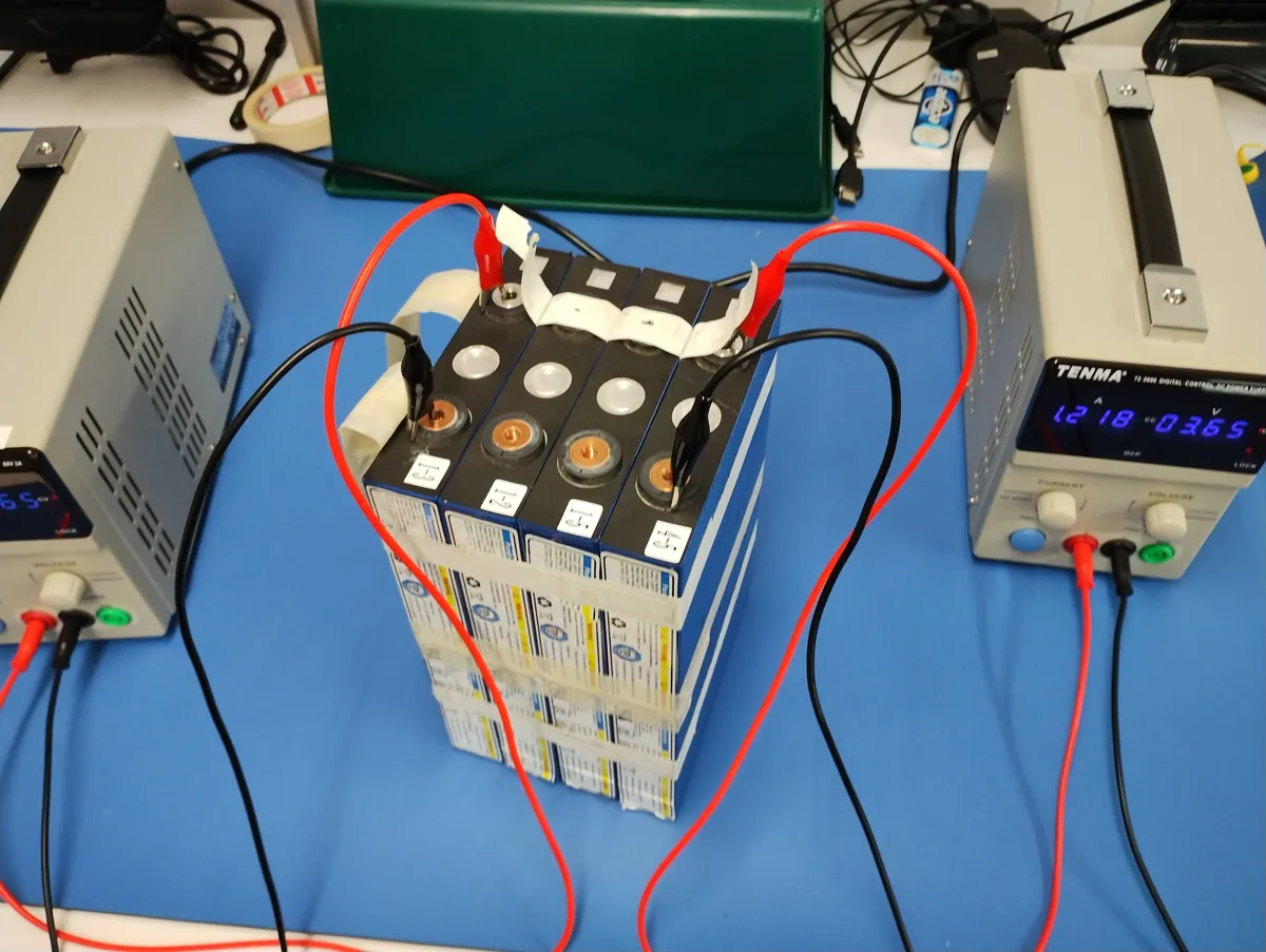 Battery pack on a blue bench between two lab power supplies with leads clipped on