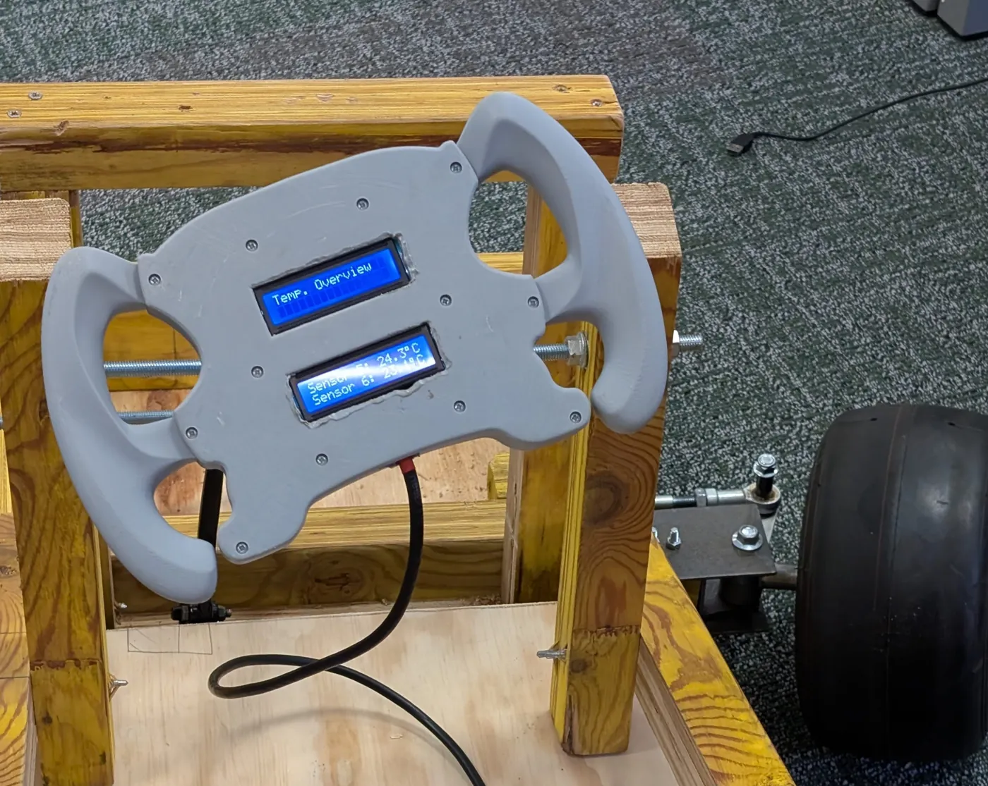 Grey 3D-printed steering wheel mounted on the wooden chassis with two blue LCDs showing a temperature overview