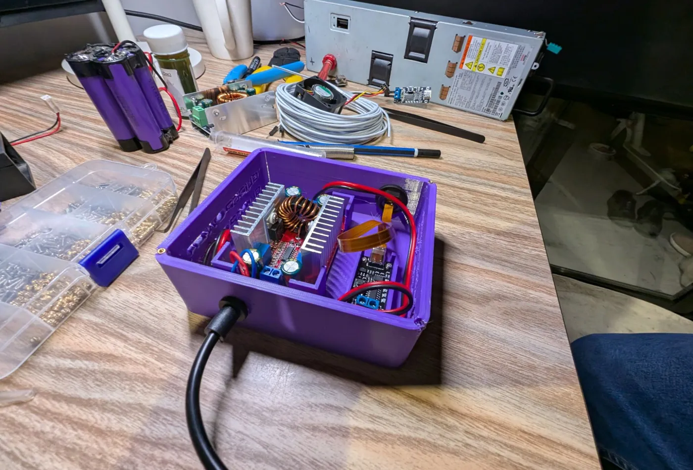 The GlidePower box open on the bench, showing the heatsinked converter board and the USB-C trigger board, with a fan, battery cells and a multimeter around it