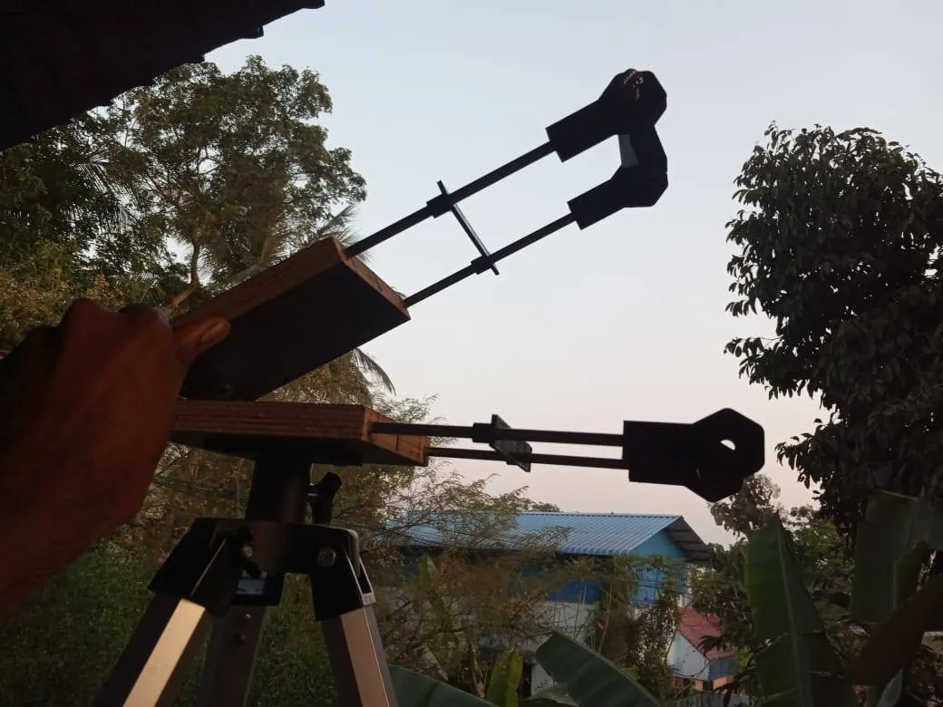 The mount held up against the evening sky, showing the two plywood plates, the hinge and the threaded rod with its stepper